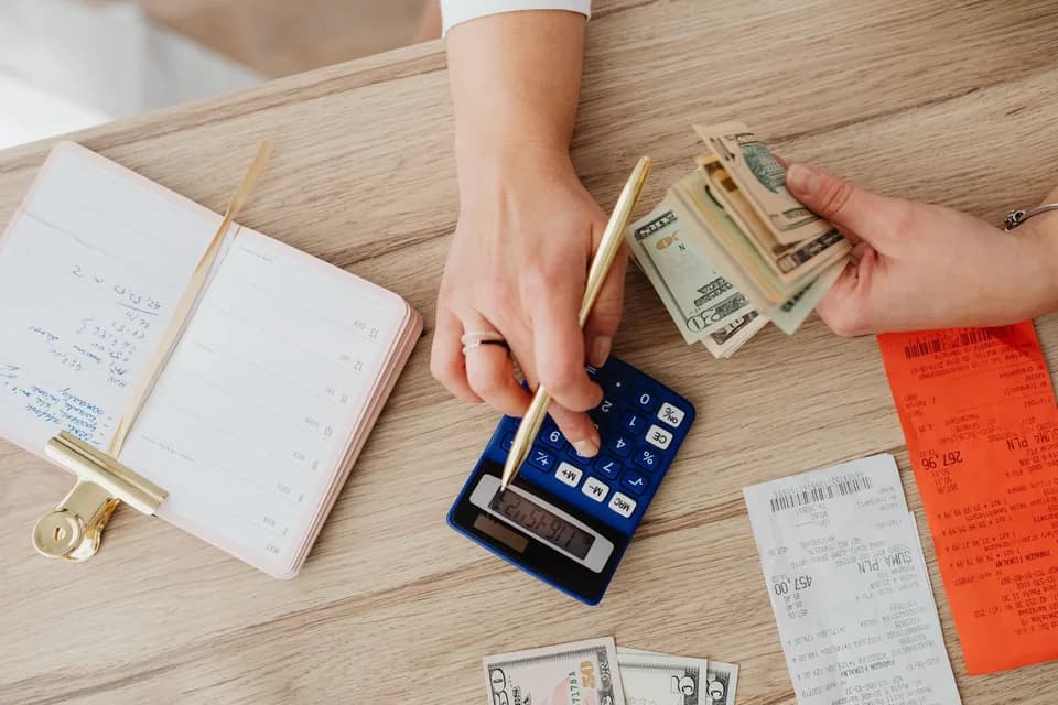 Pessoa acompanhando entradas e saídas com calculadora e anotações
